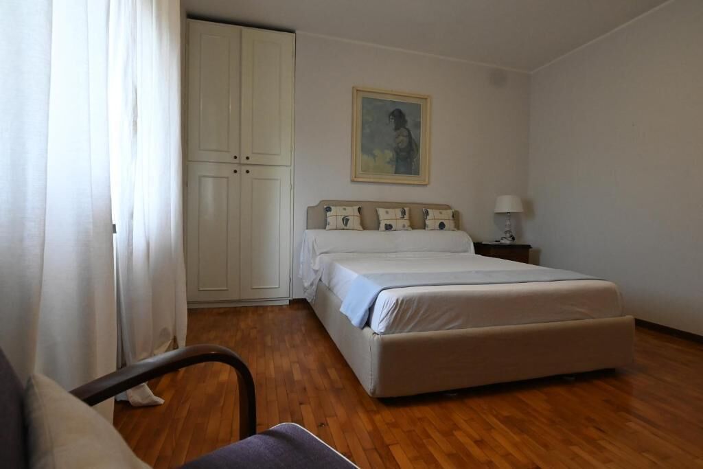 Een slaapkamer met een bed, een stoel, een kledingkast en een schilderij aan de muur.
