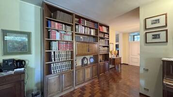 A spacious room with a large wooden bookshelf filled with books and decorative items, a wooden floor, and a door leading to another room.