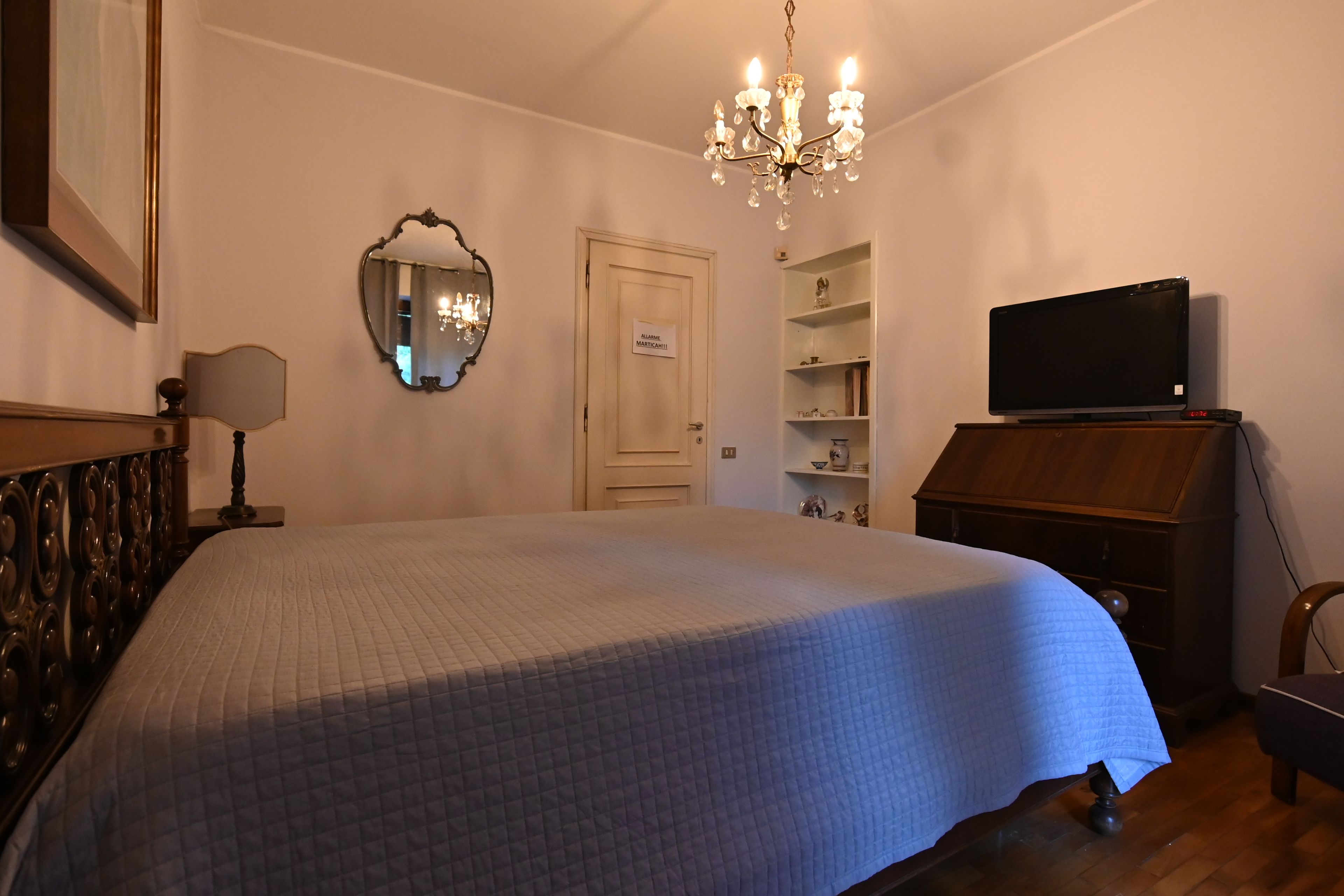 A bedroom with a large bed, a television on a stand, a mirror, and a chandelier.