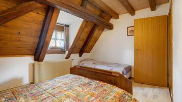 Ein Schlafzimmer mit schrägen Wänden, einem Bett mit farbenfroher Steppdecke, einem Heizkörper und einer Holztür.
