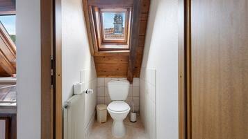 A narrow, wooden-paneled bathroom with a skylight, white toilet, and a radiator.