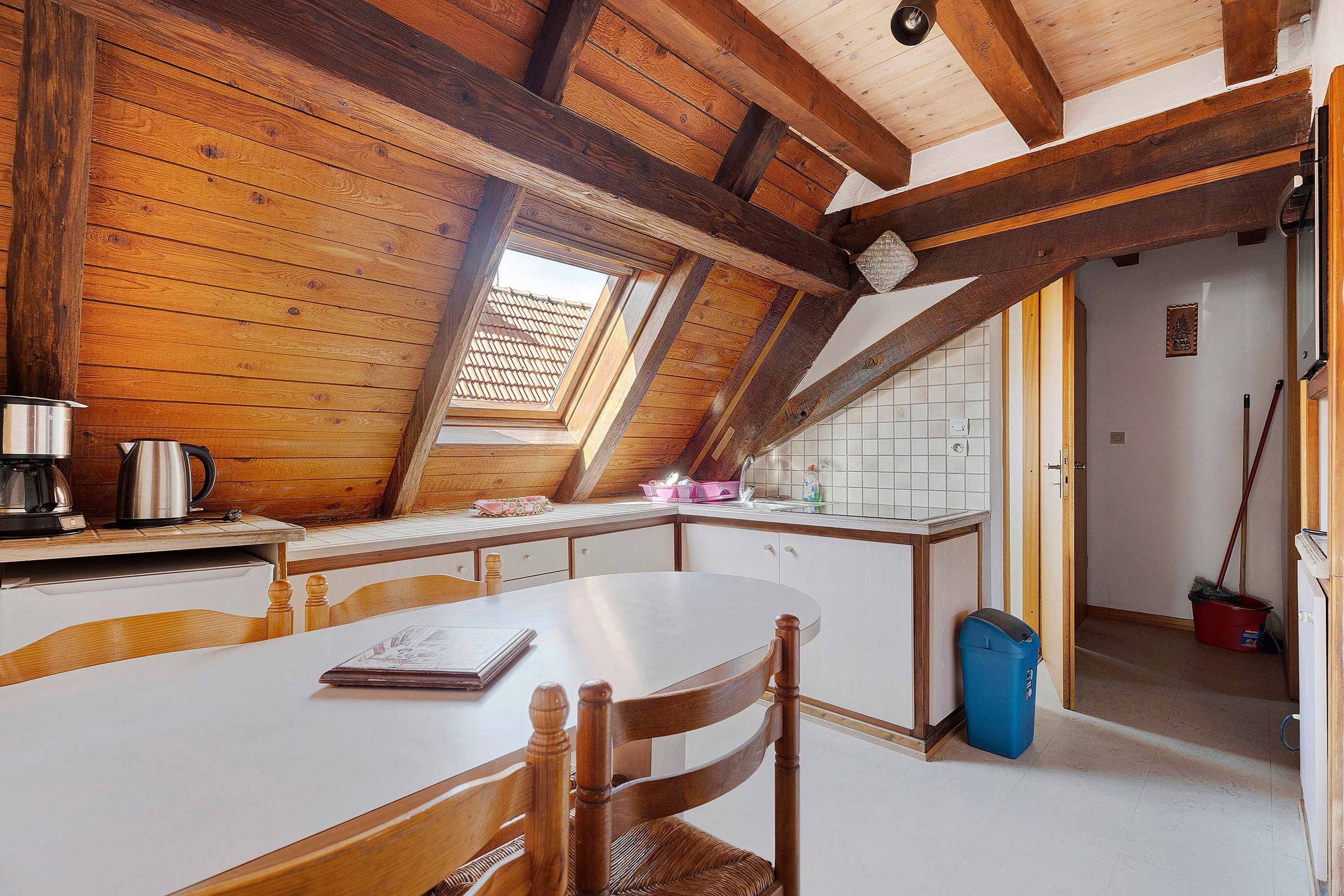 A kitchen with wooden beams, a white table, and a window.