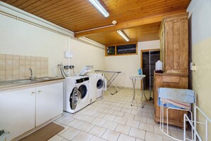A laundry room with two front-loading washing machines, a drying rack, and a small table with a towel.