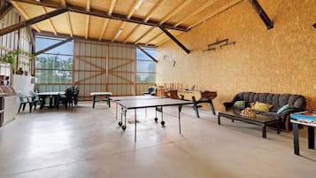 A spacious room with a high ceiling, a ping pong table, a sofa, and a dining area with chairs.