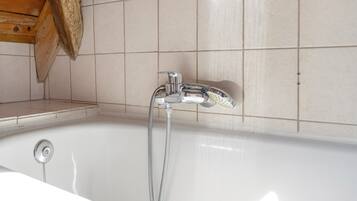 A bathroom with a bathtub, a showerhead, and a wooden shelf.