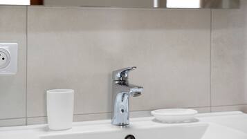 A bathroom sink with a chrome faucet, a white cup, and a soap dish.