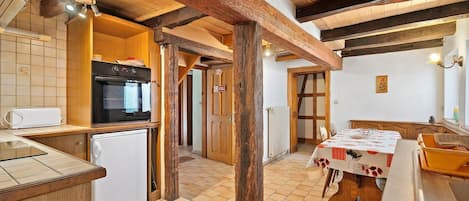 A rustic kitchen with wooden beams, a stove, a refrigerator, and a dining table set for two.