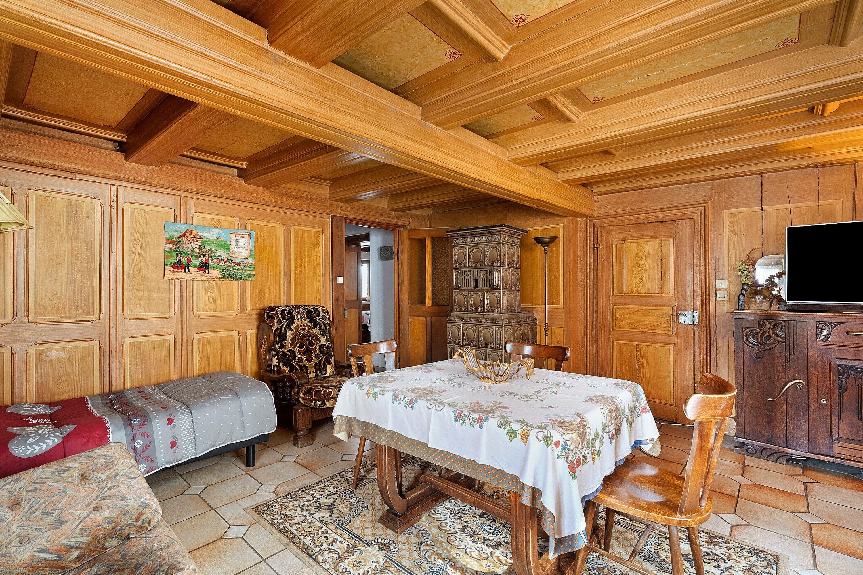 A traditional wooden interior with a dining table, chairs, a sofa, and a television on a cabinet.