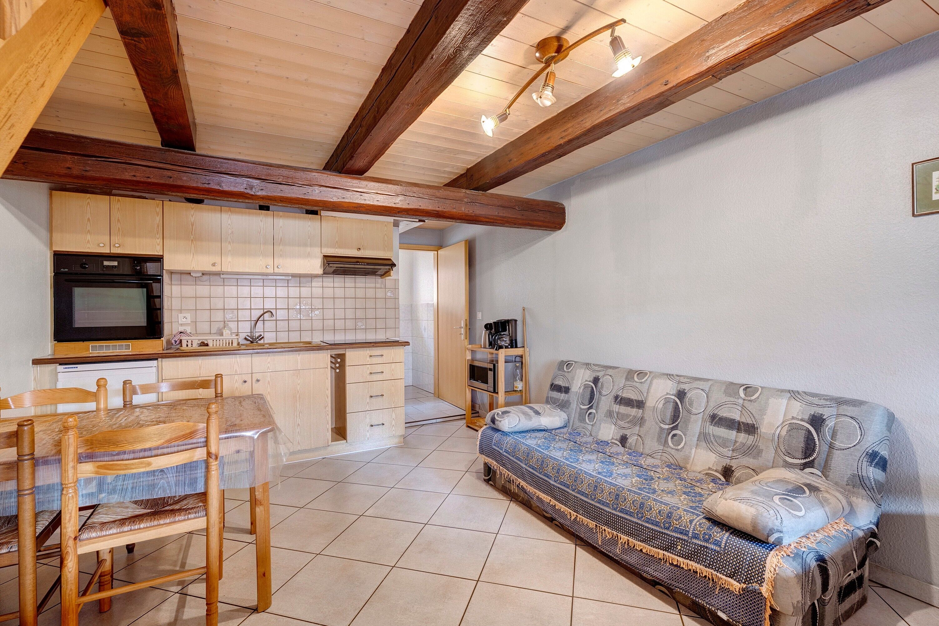 A cozy kitchen with wooden cabinets, a dining table with chairs, and a patterned sofa.