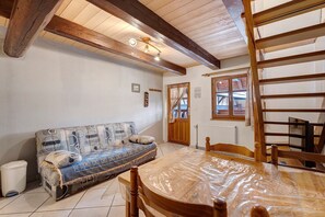 Una habitació amb sostre de fusta, un sofà, una taula amb cadires, un radiador i una finestra amb cortines.