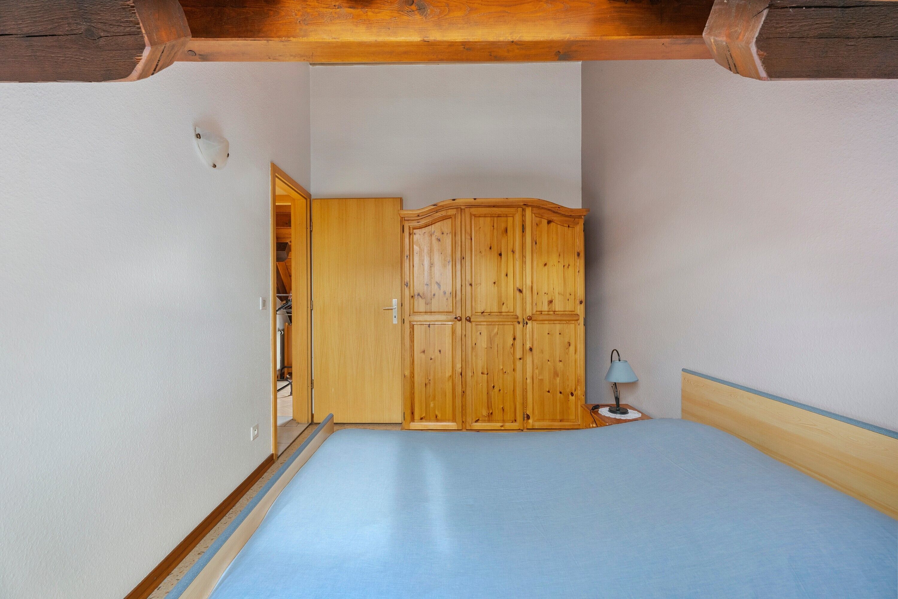 A bedroom with a bed, wooden wardrobe, and a nightstand with a lamp.
