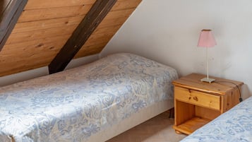 Een kleine, knusse kamer met een schuine kap, een enkel bed met beddengoed met een patroon, een nachtkastje met een lamp en een klein houten nachtkastje.
