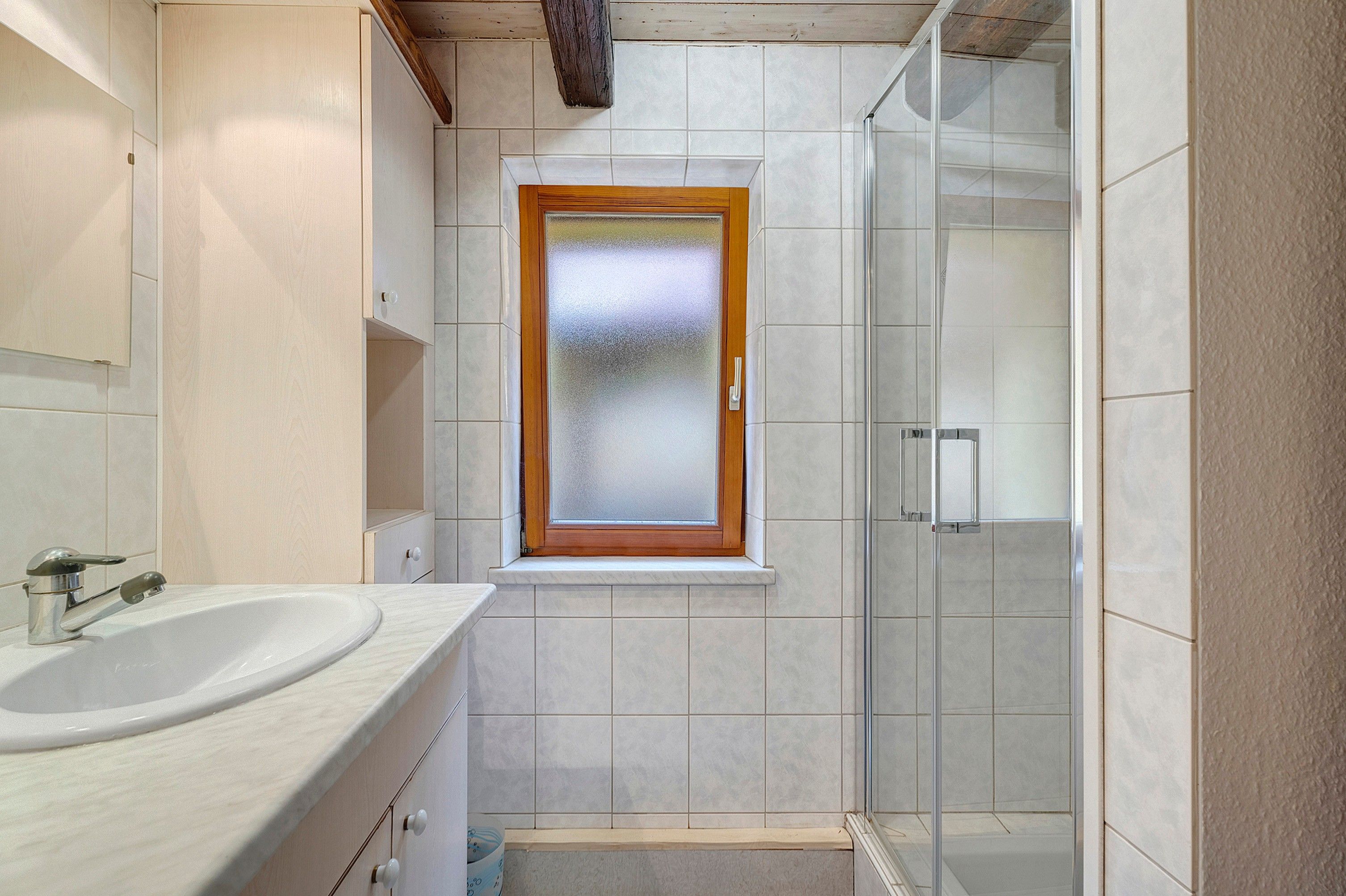 Un baño con un lavabo blanco, una ventana con marco de madera y una mampara de ducha de vidrio.