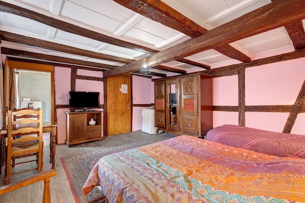 A room with exposed wooden beams, a bed with patterned bedding, a television, a wooden cabinet, and a chair.