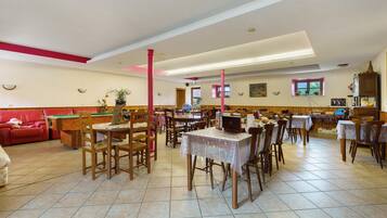 Un espace repas avec plusieurs tables et chaises, une table de billard et un canapé rouge.