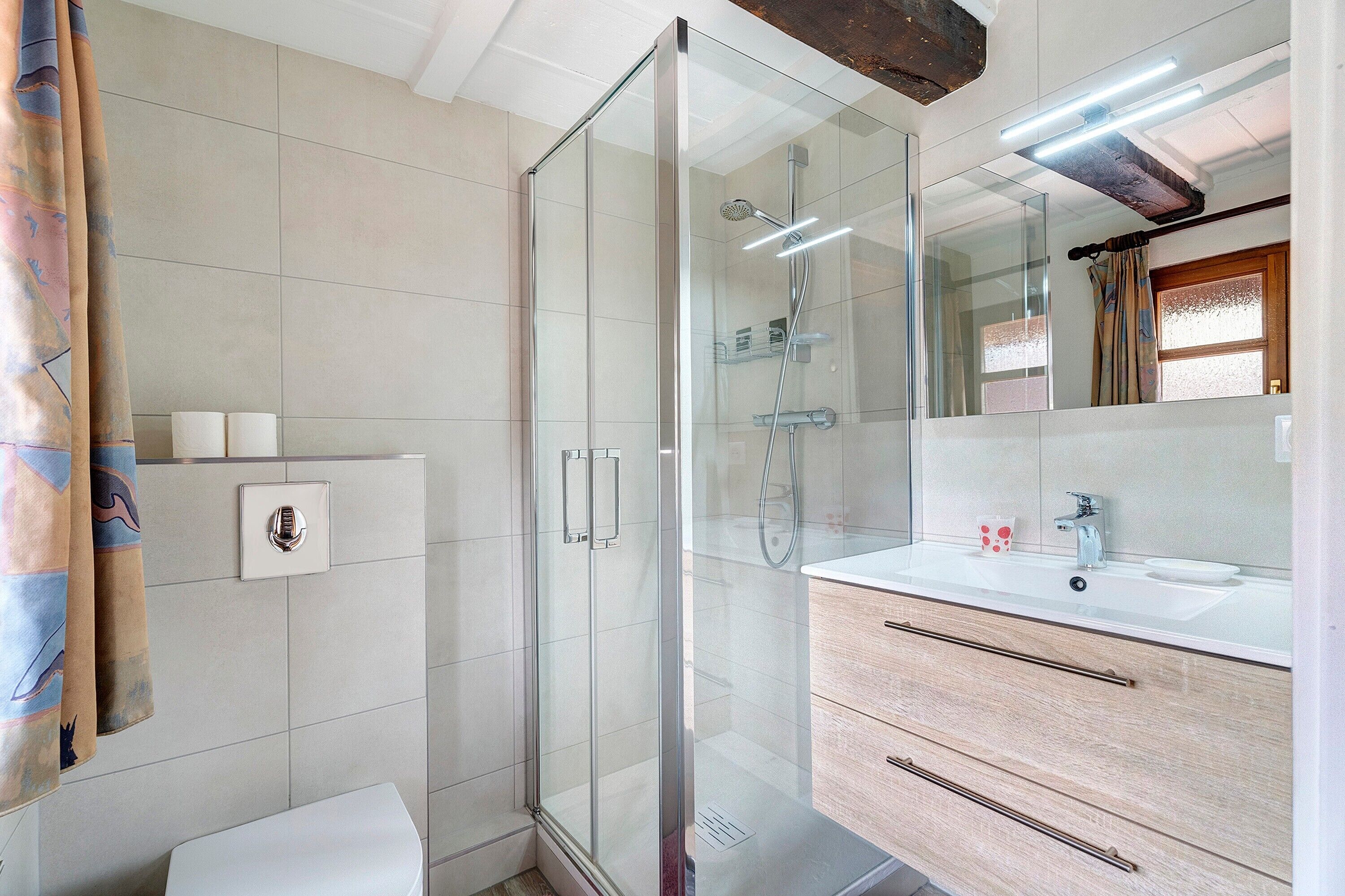 A modern bathroom with a glass-enclosed shower, a white sink with a mirror above, and a towel rack with a towel.