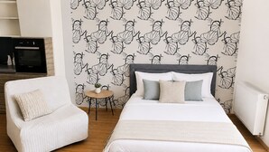 Un dormitorio con una cama, una silla, una mesita y una pared con un diseño de hojas.