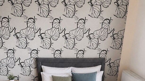 Un dormitorio con cama, almohadas, una mesita de noche y un muro con un diseño de hojas.
