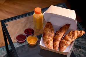 Taula de vidre amb una caixa de croissants, ampolla de suc d'aranja i petits pots de melmelada i mel.