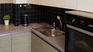 Una cocina moderna con un lavamanos de acero inoxidable, salpicadero de azulejos blanco y negro, una cafetera y un horno empotrado.