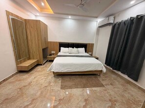Un dormitorio con cama, mesitas de noche, un armario de madera, ventilador de techo y una ventana con cortinas.