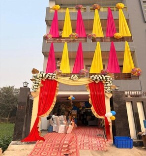 A building entrance with a red and yellow draped archway, a patterned carpet, and a blue trash bin. - BHANUDEY INN (Kesharipur)