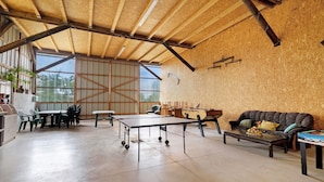 A spacious room with a high ceiling, a ping pong table, a sofa, and a dining area with chairs.