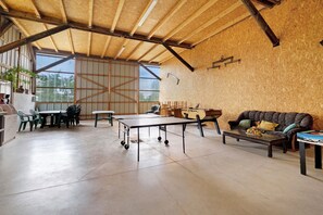 A spacious room with a high ceiling, a ping pong table, a sofa, and a dining area with chairs.