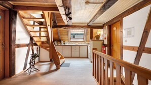 A wooden interior with a staircase leading to a loft bedroom, a kitchen area, and a small window.