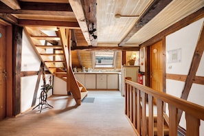 A wooden interior with a staircase leading to a loft bedroom, a kitchen area, and a small window.