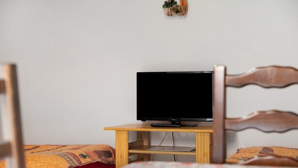 A bedroom with a bed, a wooden nightstand, and a television.