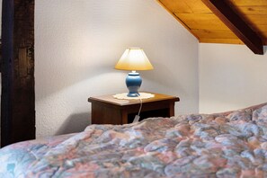 A corner of a room with a wooden nightstand holding a lamp, a patterned bedspread, and a textured wall.
