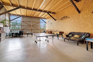 A spacious room with a high ceiling, a ping pong table, a sofa, and a dining area with chairs. - Chambre Été – Breakfast Included, Game Room – Bossendorf (Bossendorf)