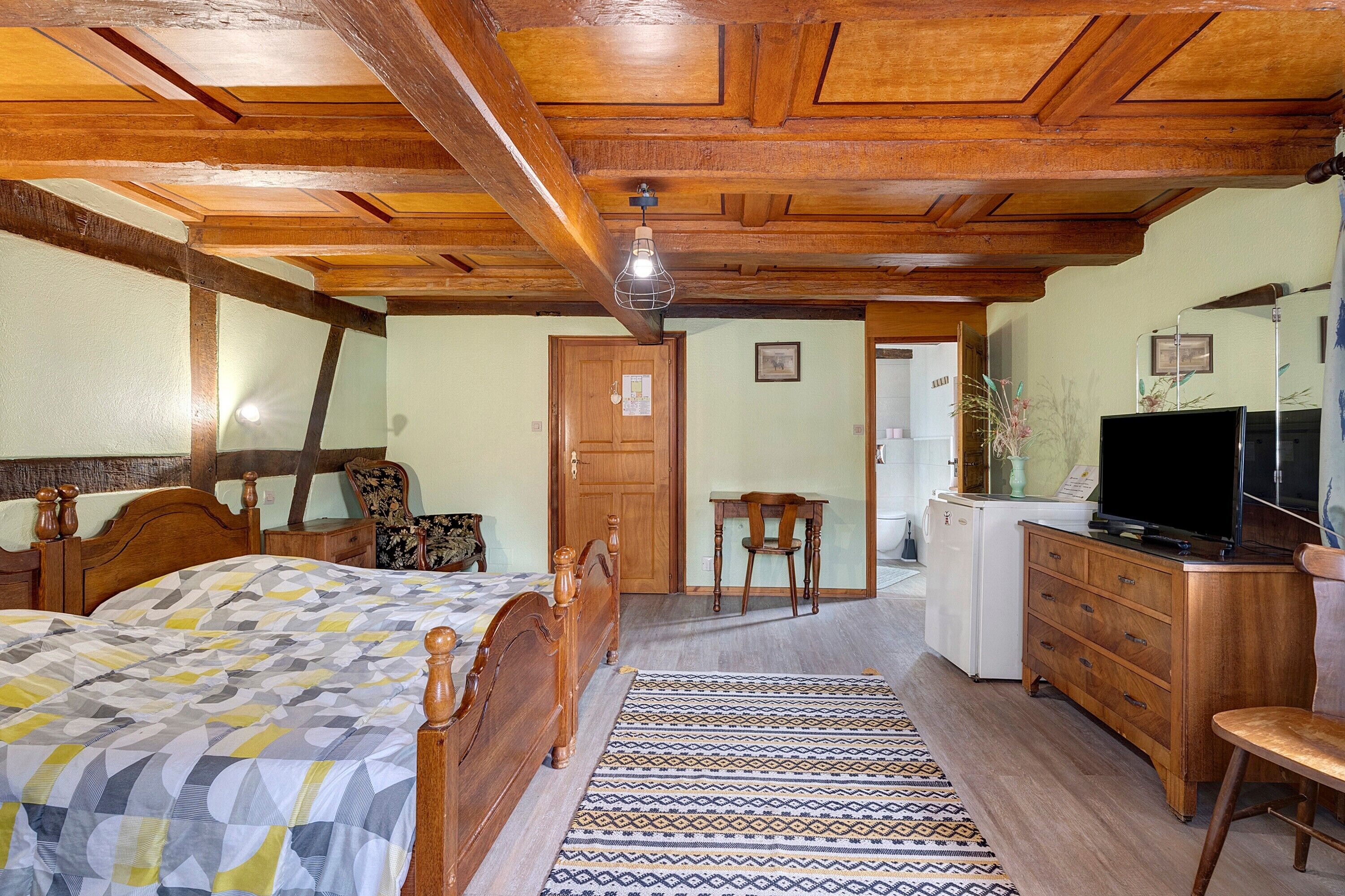 Une chambre avec un lit en bois, un bureau, une chaise, une télévision et un réfrigérateur.