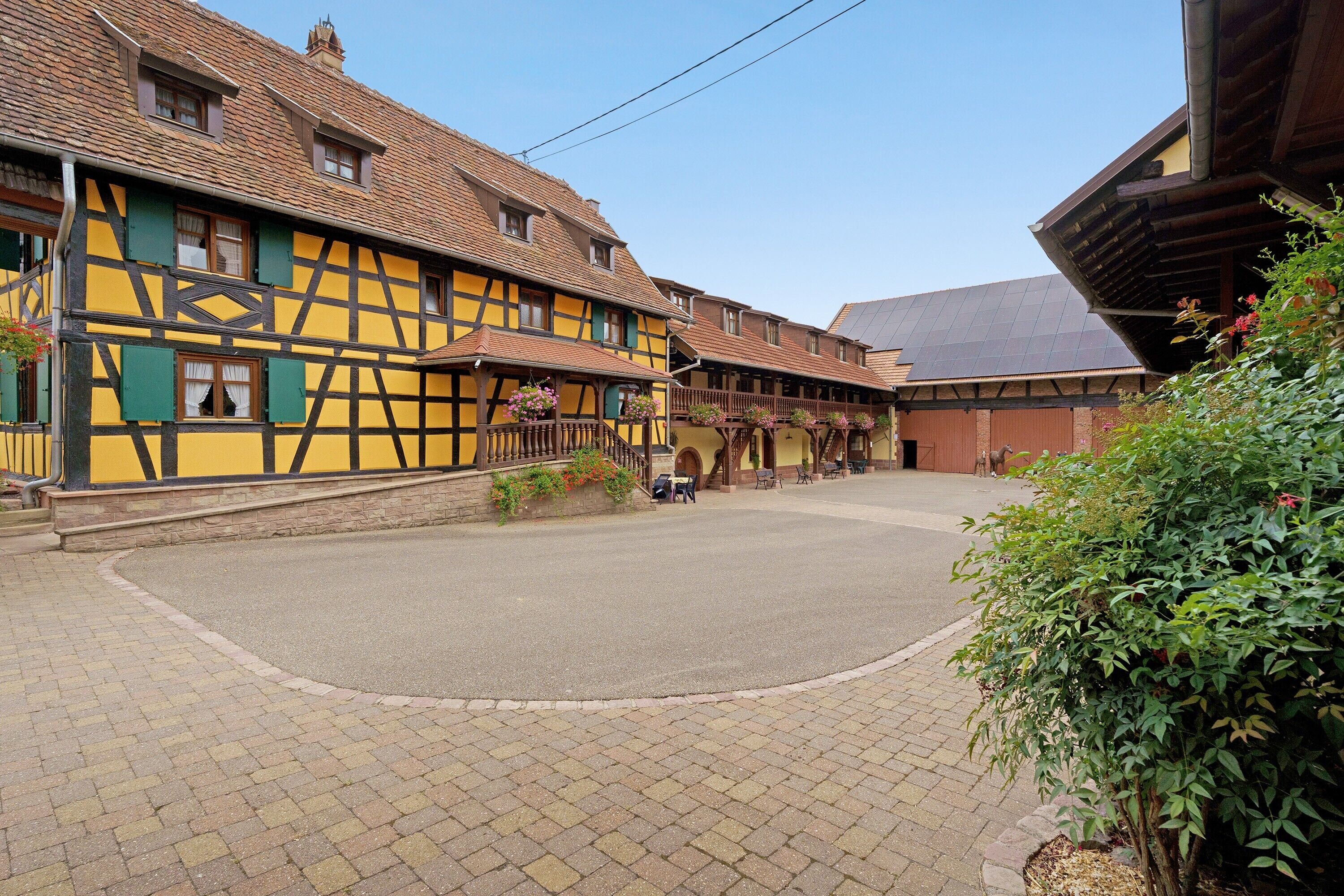 Une cour bordée de bâtiments traditionnels à colombages, un chemin pavé et un petit espace jardin.