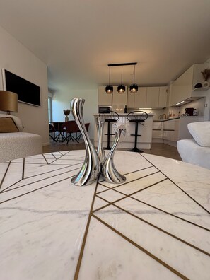 A modern kitchen with white cabinets, a dining area with a marble table, and a living room with a sofa. - Cozy Lakeside Apartment near Disneyland Paris (Serris)