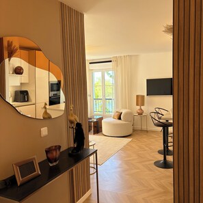 Ein modernes Wohnzimmer mit einem großen Spiegel, einem Sofa, einem Esstisch mit Stühlen und einem durch den Spiegel sichtbaren Küchenbereich.