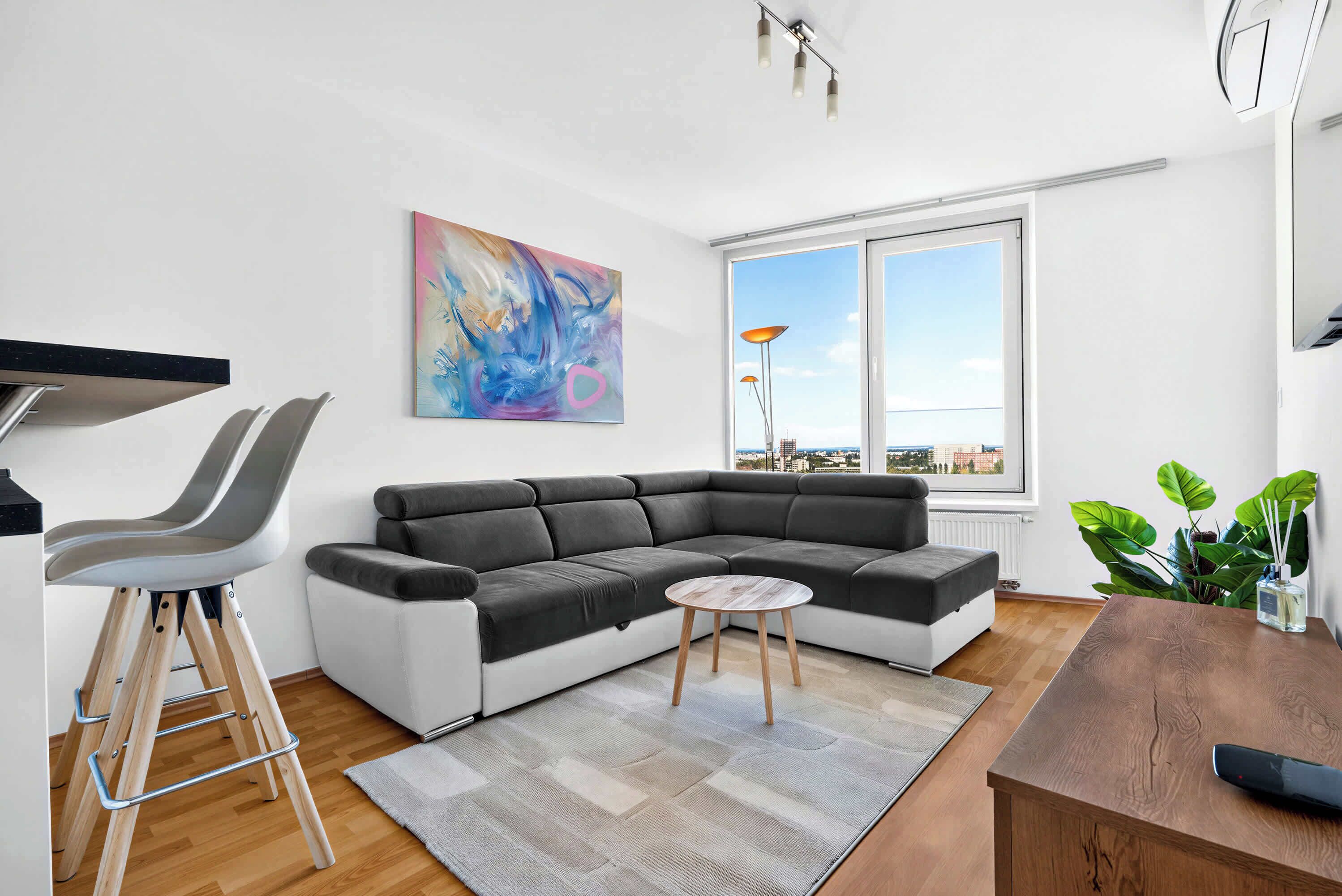 Una sala de estar moderna con un sofá modular, una mesita redonda y un ventanal con vistas a la ciudad.