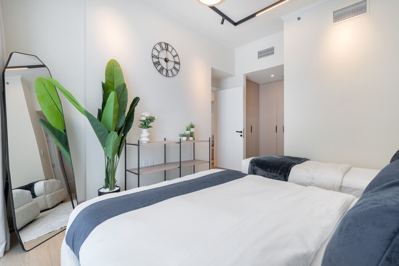 Ein modernes Schlafzimmer mit einem großen Bett, einem Nachttisch, einer Topfpflanze, einer Wanduhr und einem Kleiderschrank.