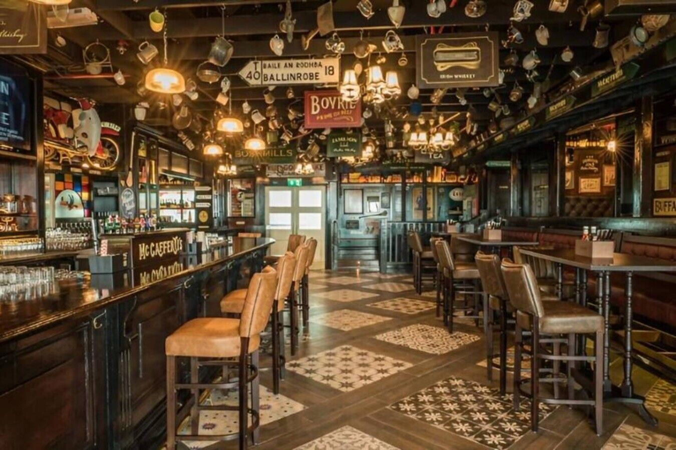 Un bar con diverse zone di seduta, una varietà di bottiglie e bicchieri sugli scaffali e insegne appese.