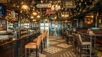 Un bar con diverse zone di seduta, una varietà di bottiglie e bicchieri sugli scaffali e insegne appese.
