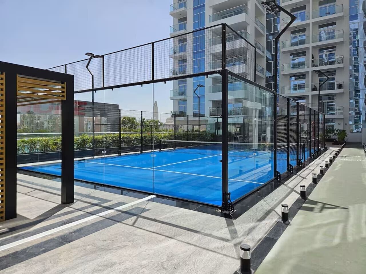 A rooftop tennis court with a net, surrounded by a glass enclosure, and adjacent to a building with multiple balconies.