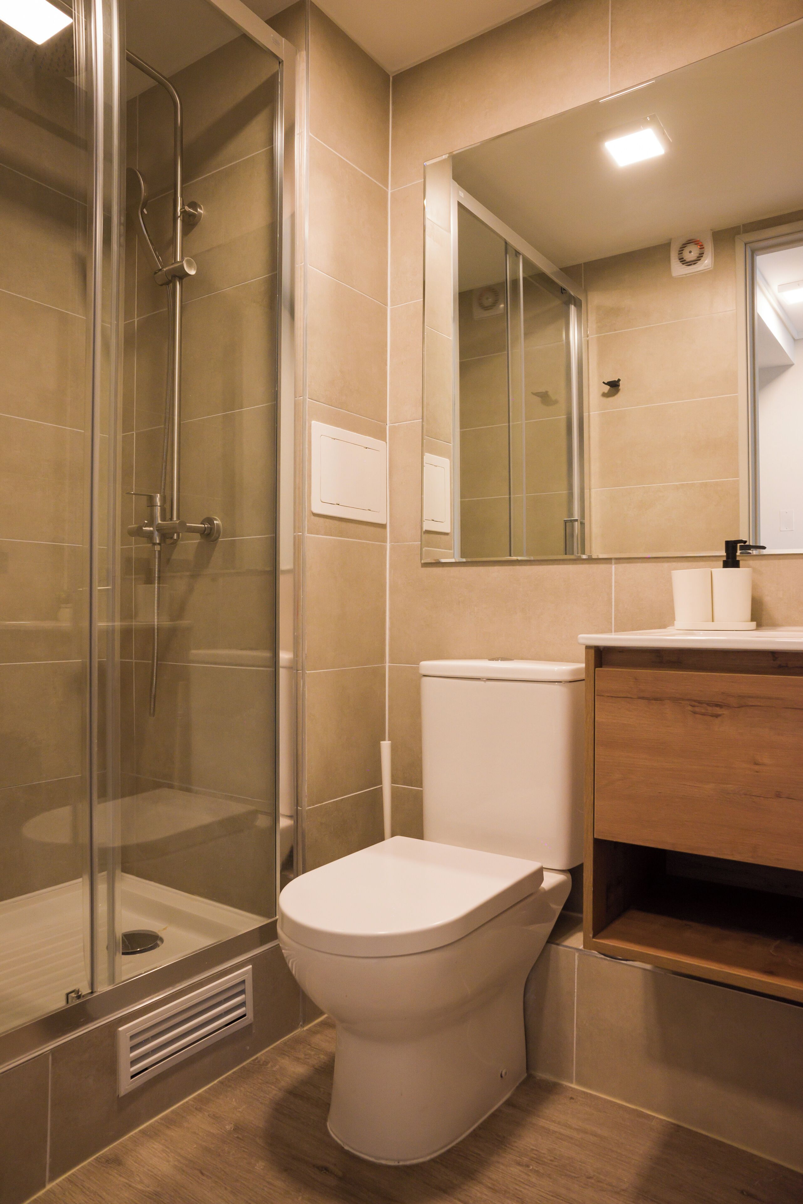 Ein modernes Badezimmer mit einer Glaskabine zur Dusche, einer Toilette und einem Holzwaschtisch mit Spiegel.
