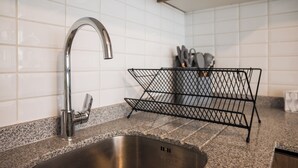 Een keuken met een roestvrijstalen spoelbak, een metalen draadrek en witte betegelde wanden.