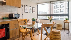 Een moderne keuken met houten kastjes, een ingebouwde magnetron, en een eethoek met een glazen tafel en stoelen.