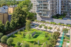 A multi-story residential building with balconies, a green park area with exercise equipment, and a pedestrian pathway. - Klimatisiertes Apartment | Parkplatz | Warschau-Wola (Warszawa)