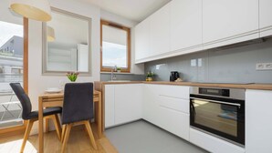 Een moderne keuken met witte kasten, een houten aanrecht, een inbouwoven en een eethoek met een tafel en stoelen.