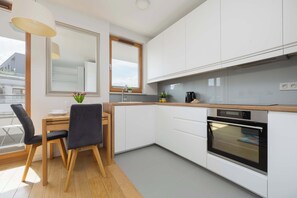 A modern kitchen with white cabinets, a wooden countertop, a built-in oven, and a dining area with a table and chairs. - Klimatisiertes Apartment | Parkplatz | Warschau-Wola (Warszawa)