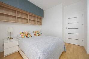 A bedroom with a bed, bedside tables, a lamp, a door, and a built-in wardrobe. - Klimatisiertes Apartment | Parkplatz | Warschau-Wola (Warszawa)