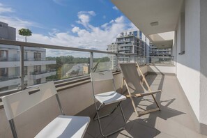 Un balcon avec deux chaises blanches et une chaise en bois, donnant sur un quartier résidentiel avec des immeubles modernes.